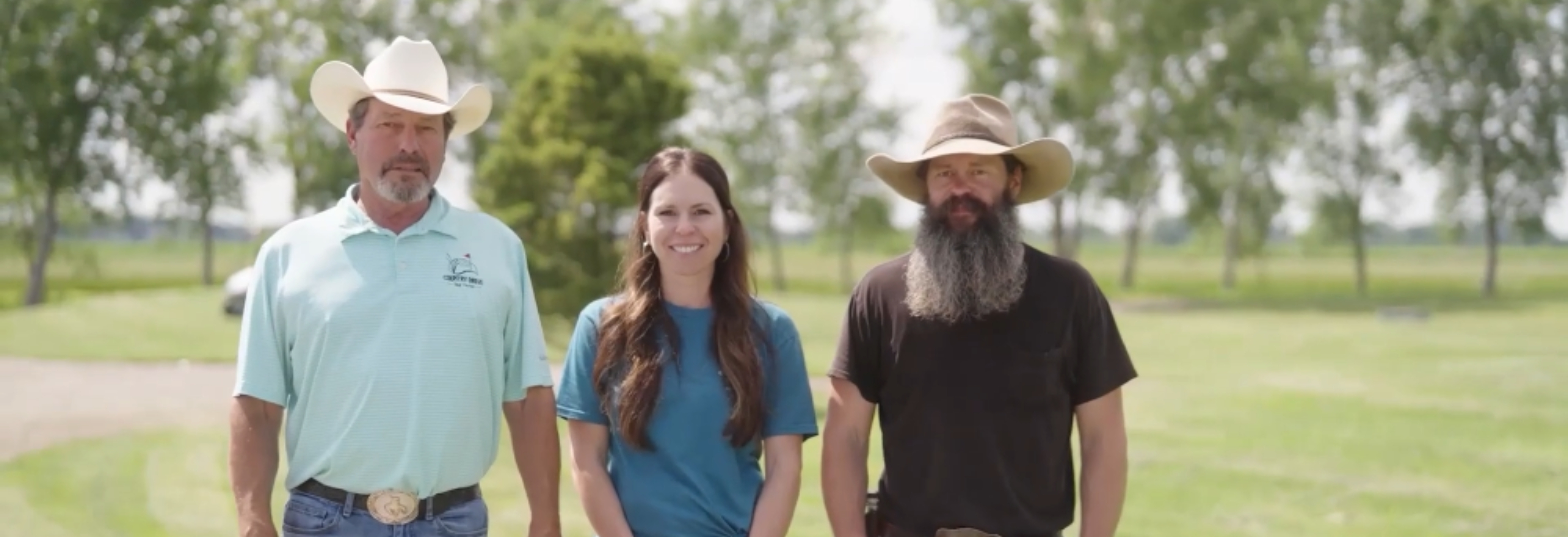 three people standing on a golf course smiling at the camera