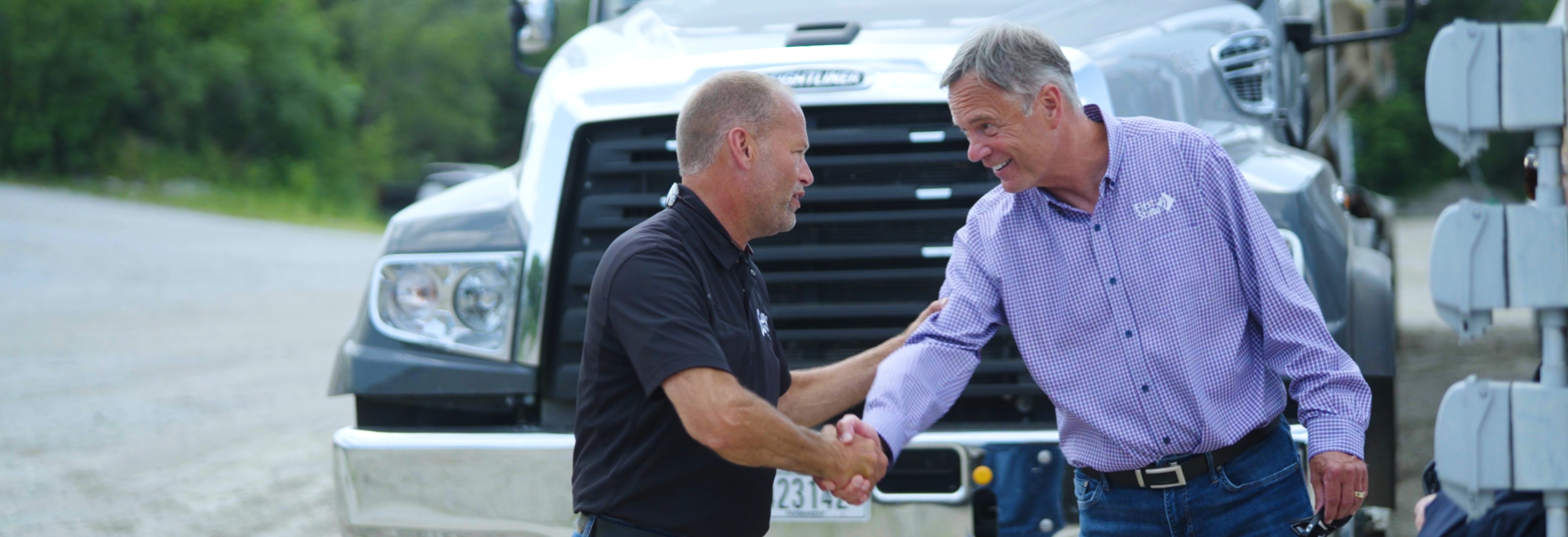 two men shaking hands in front of a semi truck