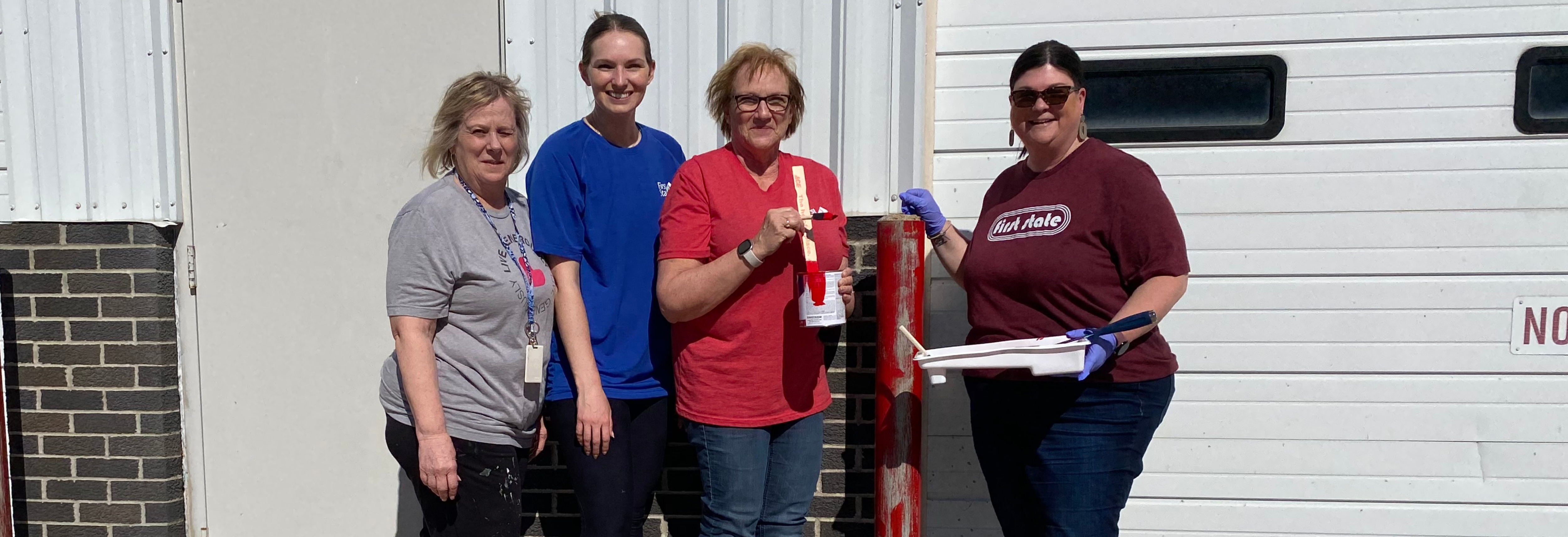 four women standing painting a pole red