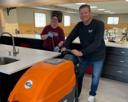 a man pushing an industrial floor cleaner and a woman sweeping