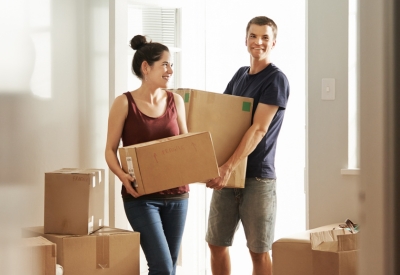 young man and woman carrying boxes into house