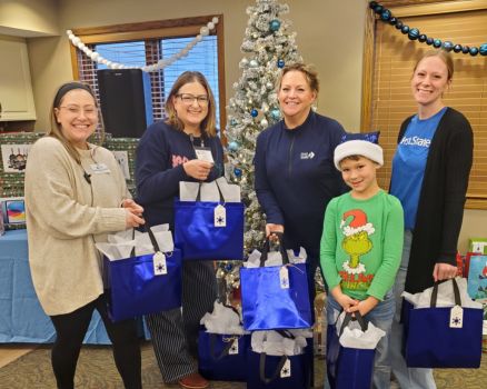 four women holding gift bags in front of a Christmas Tree