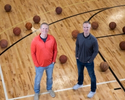 two men standing on a basketball court looking up with basketballs around them